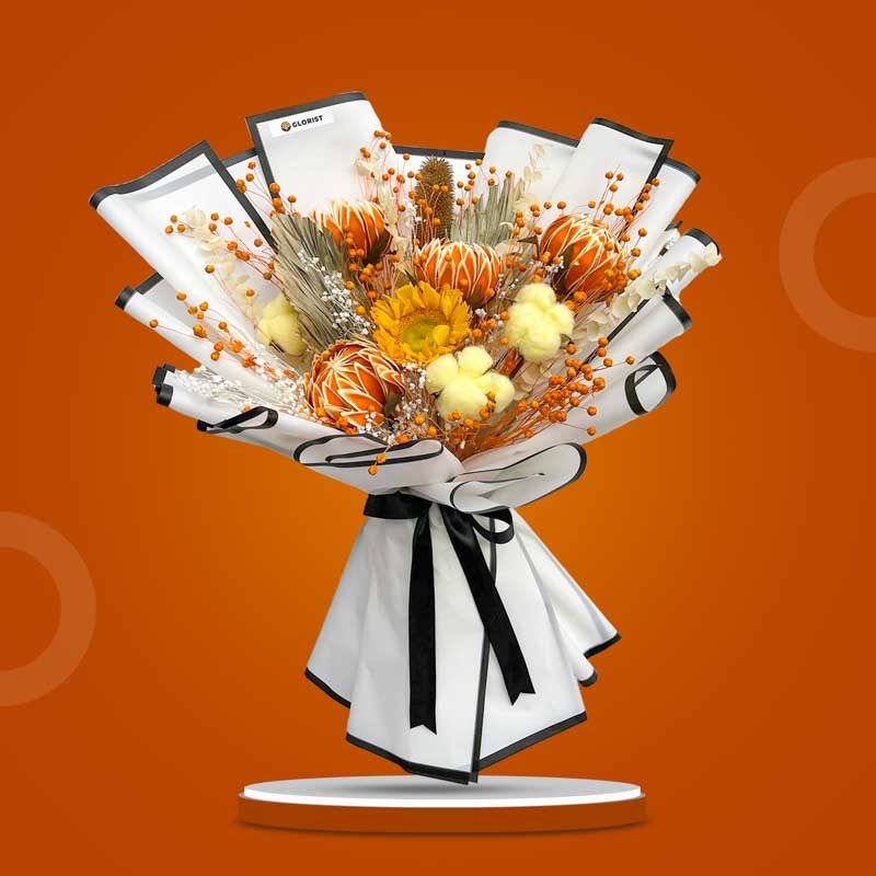 Carnelian Timeless dried bouquet with orange Jimba flowers, sunflower, yellow cotton heads, bleached eucalyptus, Valentine fruit, and anahaw in white-bordered black-edge wrap