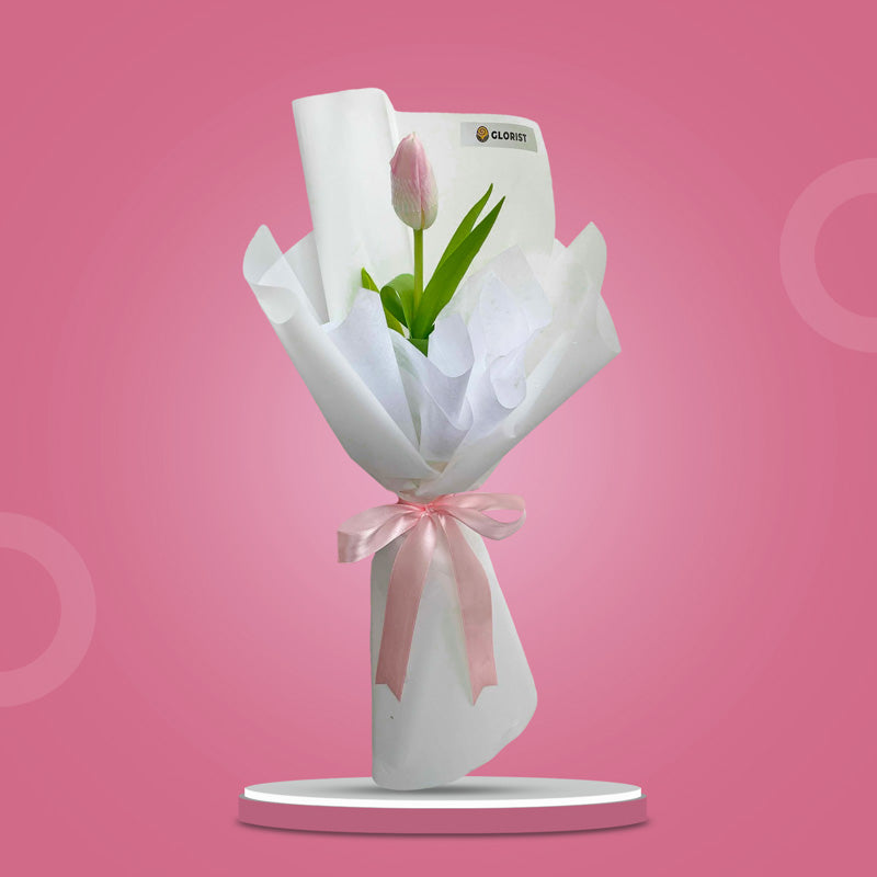 Fine Perennial bouquet with a light pink tulip in layered white Korean and non-woven wrap tied with a light pink ribbon