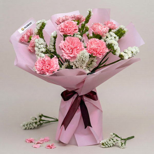 Mellow Radiance bouquet with 10 light pink carnations and white statice in light pink Korean wrap with brown ribbon