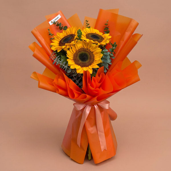 Zestful Summer bouquet with three sunflowers and eucalyptus in orange Korean wrap tied with salmon ribbon