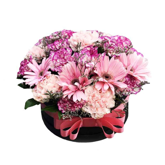 Charming box filled with two-tone violet and light pink carnations, complemented by pink gerberas and accented with misty blue fillers, creating a delightful and colorful floral arrangement.