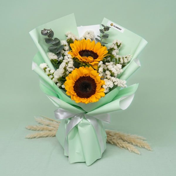 Attractive Summer bouquet with two sunflowers, eucalyptus baby blue, and statice in matcha green wrap with white ribbon