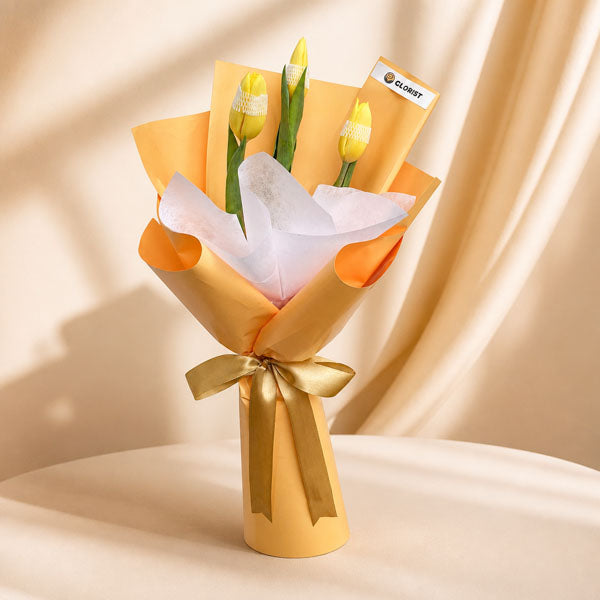 Authentic Perennial bouquet with three yellow tulips in yellow-orange and white wrap tied with light gold ribbon