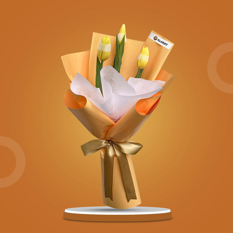 Authentic Perennial bouquet with three yellow tulips in yellow-orange and white wrap tied with light gold ribbon