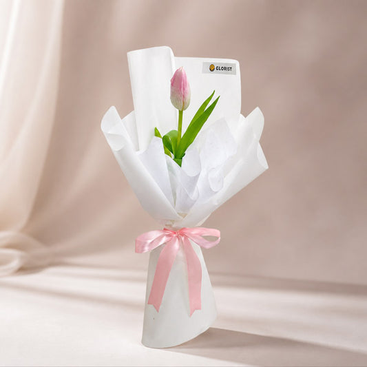Fine Perennial bouquet with a light pink tulip in layered white Korean and non-woven wrap tied with a light pink ribbon