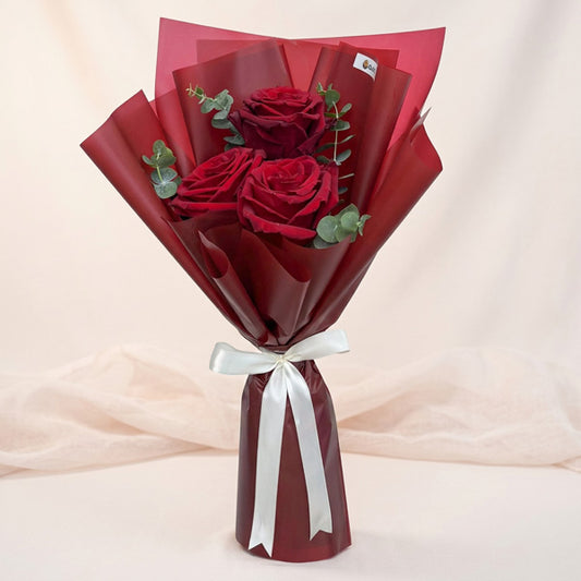 Luna Dreamland bouquet with 3 red Ecuadorian roses and eucalyptus baby blue in maroon wrap tied with a cream ribbon
