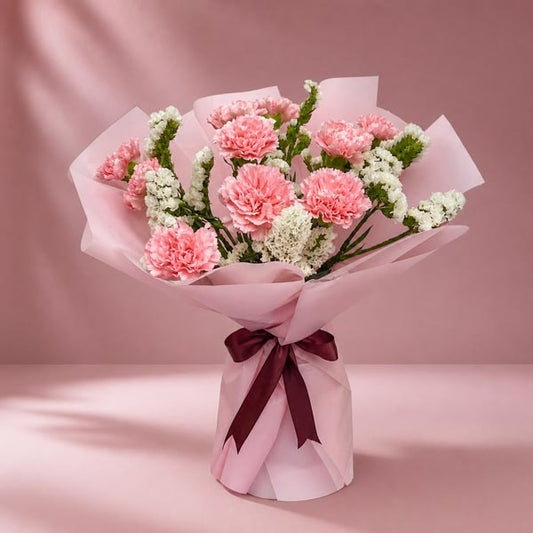 Mellow Radiance bouquet with 10 light pink carnations and white statice in light pink Korean wrap with brown ribbon