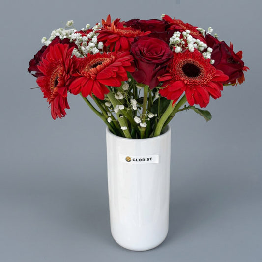 Red China roses and red gerbera daisies with gypsophila baby's breath in a white glass vase, a bold mixed flower gift with same-day Metro Manila delivery