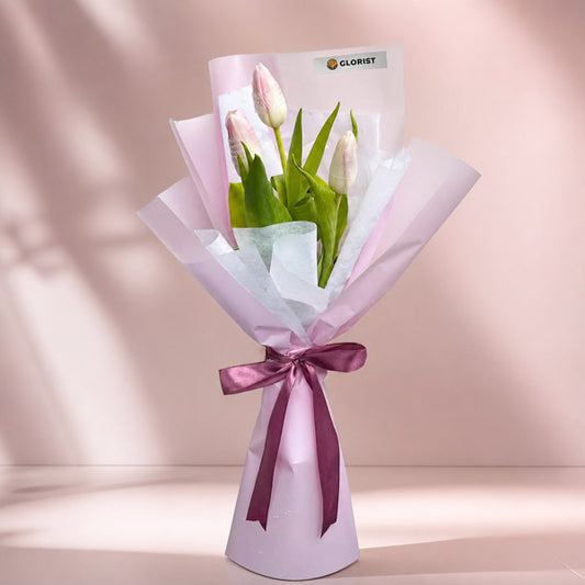 Treasured Perennial bouquet with three light pink tulips in light violet and white wraps tied with an old rose ribbon